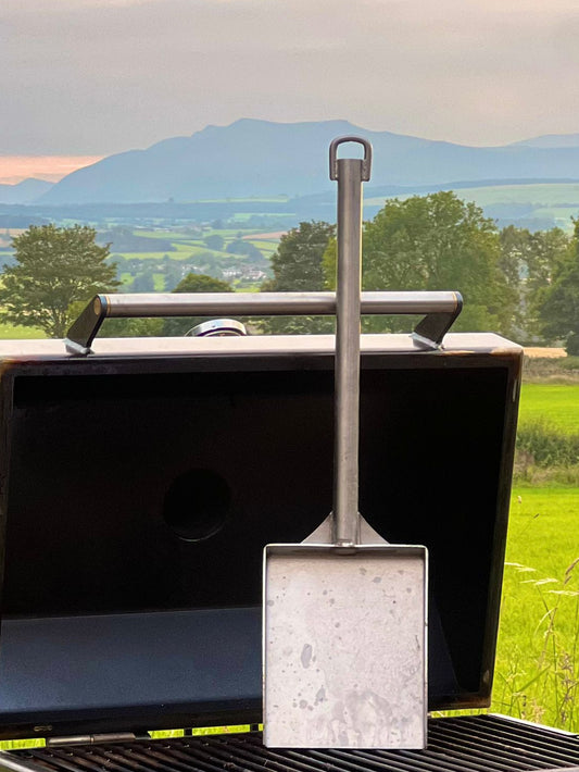 Metal shovel on a grill with a scenic background of mountains and green fields.